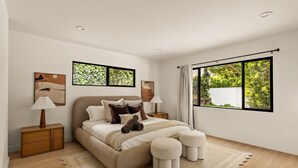 A modern bedroom with a large bed, two bedside tables, a window with a view of greenery, and artwork on the walls. - Executive 4BR/4BA Home Near Universal Studios (Los Angeles County)