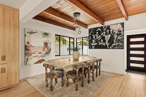 A dining area with a wooden table and chairs, large abstract paintings, and a view of the outdoors.