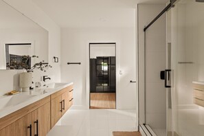 A modern bathroom with a glass shower enclosure, a white vanity with a large mirror, and a wooden cabinet. - Executive 4BR/4BA Home Near Universal Studios (Los Angeles County)