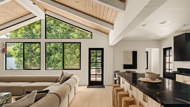A modern kitchen with a large island, a dining area with a sofa, and large windows with a view of trees. - Executive 4BR/4BA Home Near Universal Studios (Los Angeles County)
