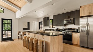 A modern kitchen with a large island, dark cabinetry, stainless steel appliances, and a wooden ceiling. - Executive 4BR/4BA Home Near Universal Studios (Los Angeles County)
