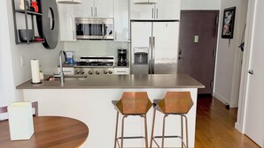 A modern kitchen with stainless steel appliances, a central island with bar stools, and a dining table with chairs.