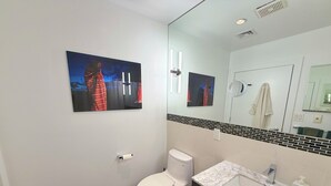 A modern bathroom with a toilet, sink, and a large mirror. There are two framed pictures on the wall.