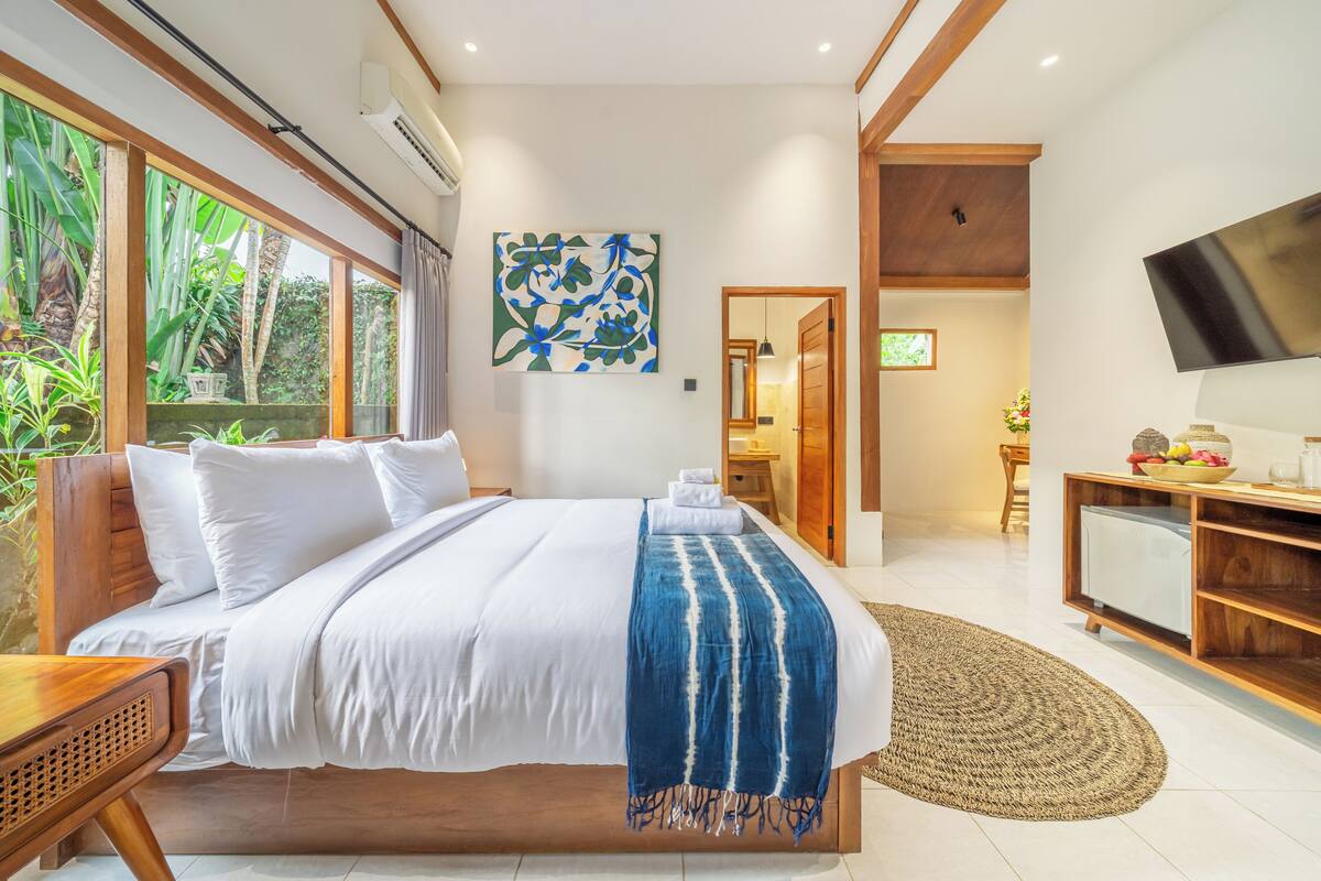 Un dormitorio con cama, televisión, escritorio y vistas a zonas verdes.