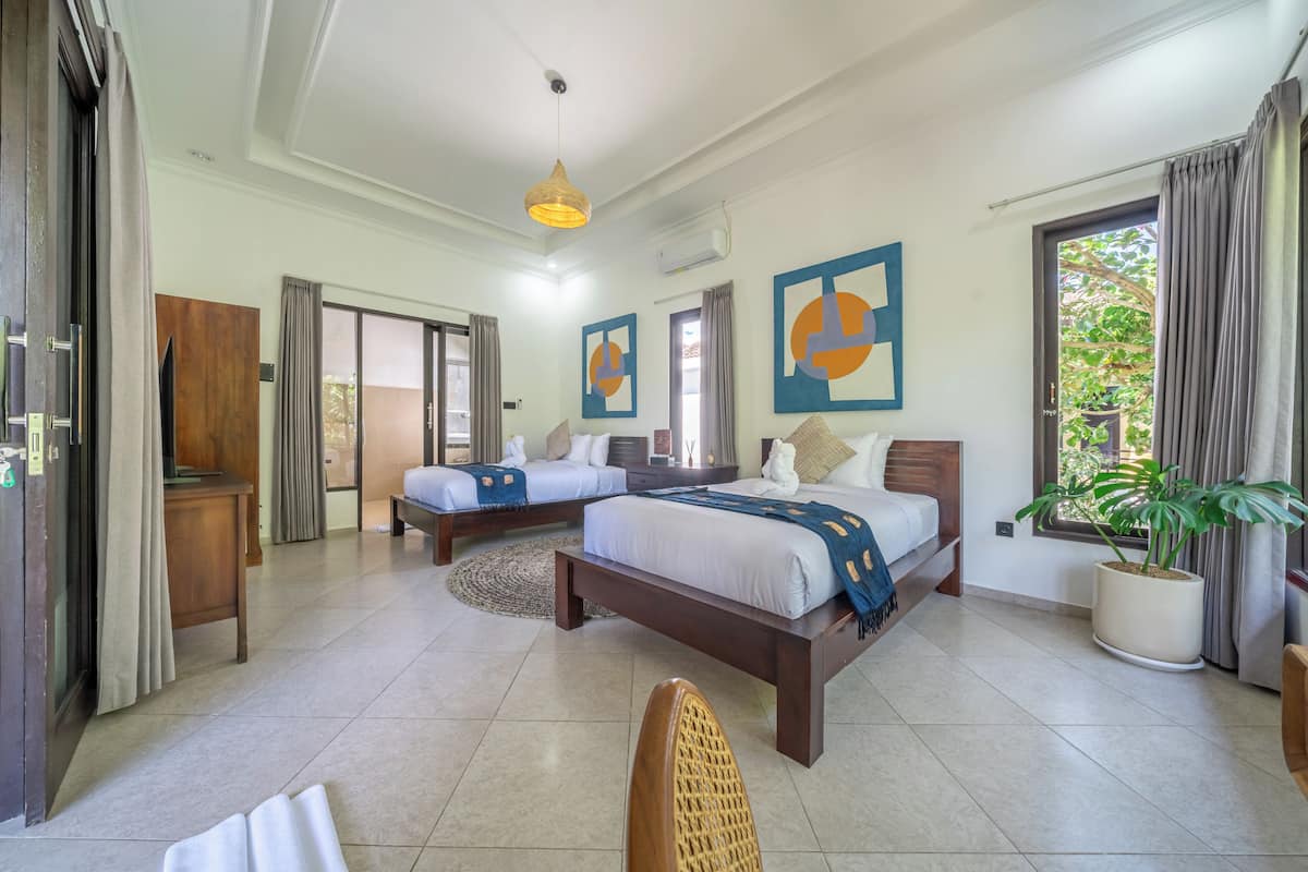 Habitación de hotel con dos camas, un ventanal grande, una planta en maceta y obras de arte en las paredes.