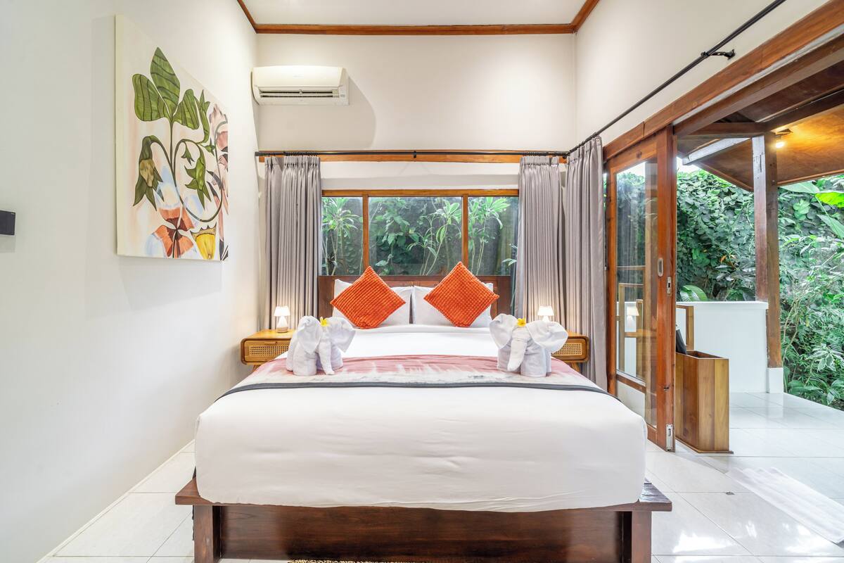 Habitación de hotel con una cama grande, un cuadro en la pared y vistas a la vegetación por la ventana.