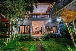 Una casa moderna con un espacio central de estar integrado, un balcón y exuberante vegetación tropical.