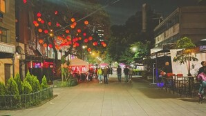 Straßenszene bei Nacht mit gepflastertem Bürgersteig, roten Laternen und Außenbereichen zum Sitzen.