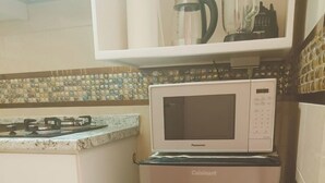 Eine Küchenzeile mit Mikrowelle, einem Zwei-Türen-Kühlschrank, einem Gasherd und einem Mülleimer.
