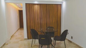 Ein Zimmer mit einer Holztür, die sich verschieben lässt, einem Glastisch mit Stühlen und einem gefliesten Boden.