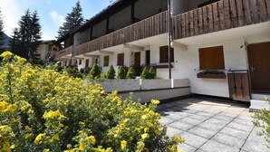 Et hotel med et overdækket udendørsområde, træbalkoner og en have med gule blomster.