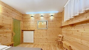 Et rum med træpaneler, seng, radiator, et lille bord og et vindue med et spejl.