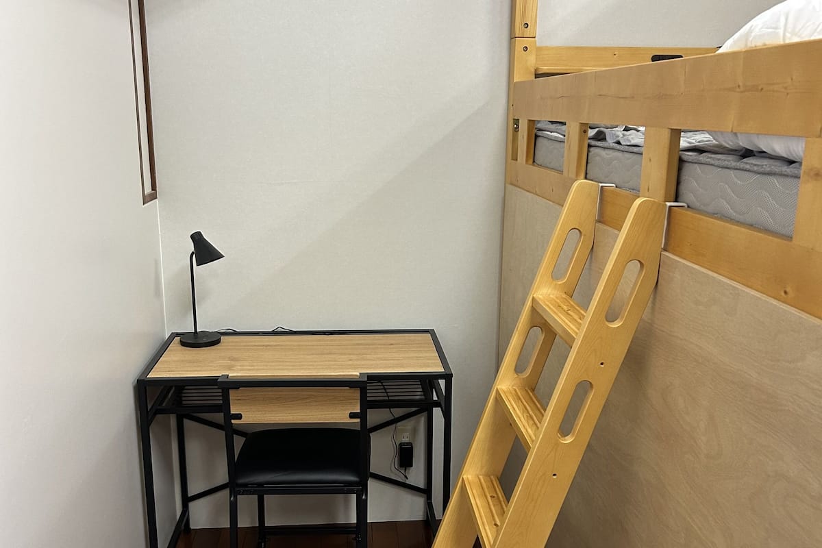 Una litera con escritorio y silla, un cubo de basura pequeño y una escalera.