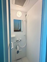 Un box de ducha pequeño y cerrado con cabezal de ducha manual, un accesorio de ducha manual y un espejo instalado en la pared.