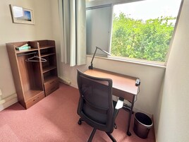 Una habitación con escritorio, silla, armario y ventana con vistas a zonas verdes.