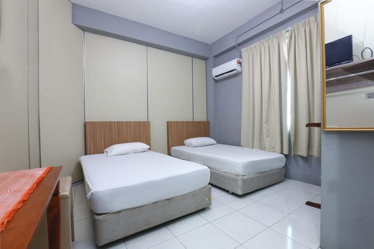 A hotel room with two single beds, a wardrobe, an air conditioning unit, a mirror, and a television.