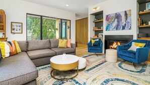 Ein modernes Wohnzimmer mit einer Eckcouch, einem runden Couchtisch, einem blauen Sessel, einem Kamin und einem großen abstrakten Gemälde.
