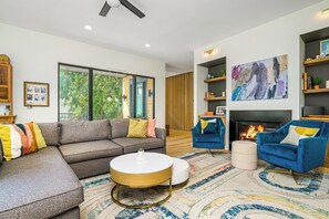 A modern living room with a sectional sofa, a round coffee table, a blue armchair, a fireplace, and a large abstract painting. - 5 Bdr/5ba Luxury new build near downtown and walkable to bars and restaurants (Kansas City)