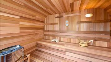 A wooden sauna with benches, a bench heater, and a bucket.