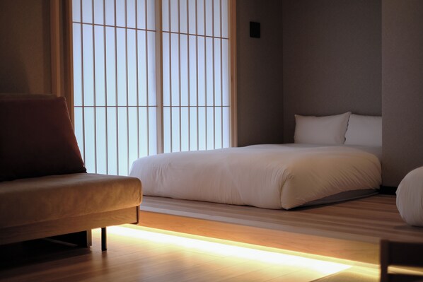 A modern bedroom with a bed, a sofa, and a window with vertical blinds. - TOUSUMI (Fukuoka)