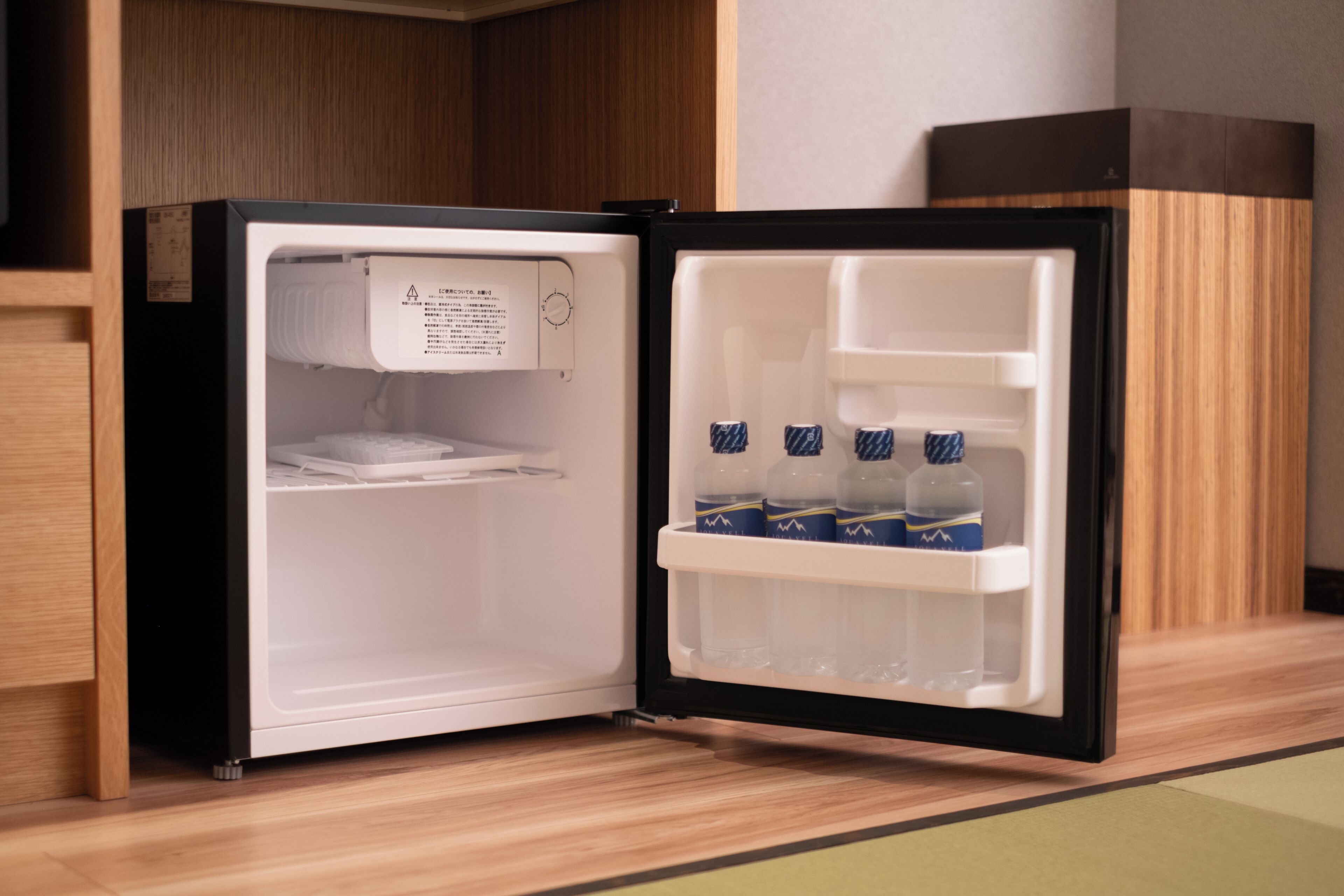 A refrigerator with a warning label, a freezer compartment, and a shelf with bottled water.