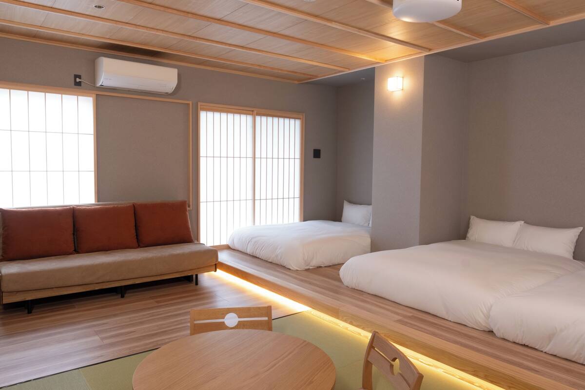 Ein Zimmer mit einer Couch, zwei Betten, einem Tisch und einem Deckenventilator.