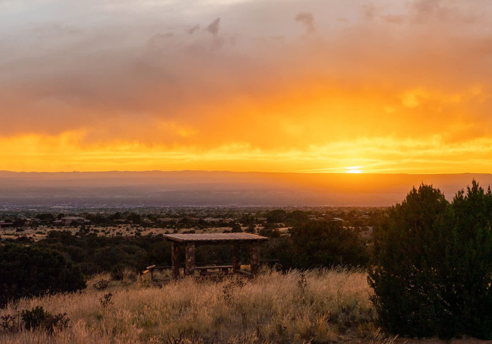 A sunset view with a clear sky, a distant cityscape, and a small structure in the foreground.