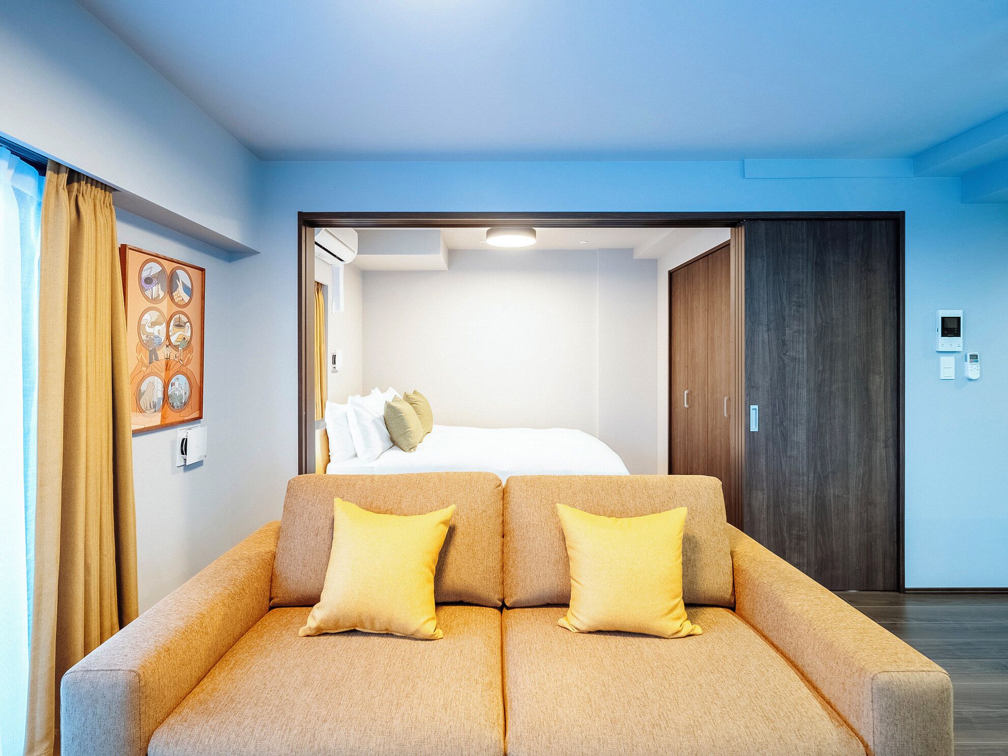 A hotel room with a sofa, a bed, a wardrobe, and a wall-mounted air conditioning unit.