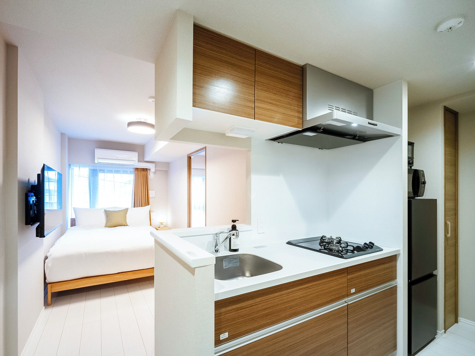 A compact hotel room with a bed, a kitchenette, and a bathroom.