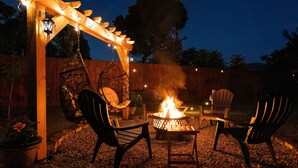 Een terras met vuurkorf, stoelen en een pergola met lichtjes.