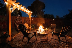 Eine Terrasse mit Feuerstelle, Stühlen und einer Pergola mit Lichterketten.