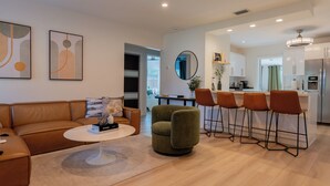 Een moderne woonkamer met een bank, salontafel en barstoelen. Er is een keuken met een koelkast en een eettafel.