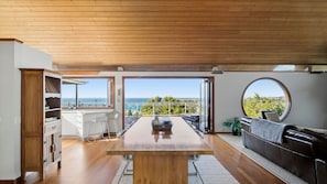 A spacious kitchen with a large wooden table, a bar area, and a view of the ocean. - Wind Dancer Retreat in Kiama (Kiama)