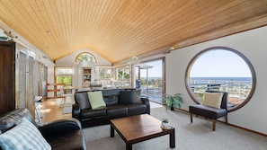 A spacious living area with a high ceiling, a large round window offering a view of the sea, and a cozy seating arrangement. - Wind Dancer Retreat in Kiama (Kiama)
