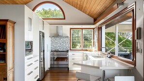 A modern kitchen with a large window, a built-in stove, and a wooden ceiling. - Wind Dancer Retreat in Kiama (Kiama)
