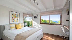 A bedroom with a bed, a desk, a chair, a window with a view, and artwork on the wall. - Wind Dancer Retreat in Kiama (Kiama)