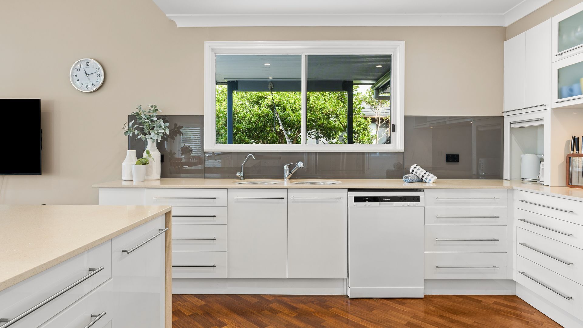 A modern kitchen with a window, white cabinetry, a dishwasher, and a clock on the wall.