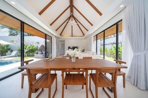 Un vaste espace dédié à la salle à manger, avec une table et des chaises en bois, de grandes fenêtres et une vue sur l’extérieur.