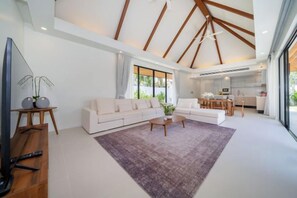 Un vaste espace de vie comprenant un grand canapé, une table basse et un téléviseur posé sur un meuble en bois.