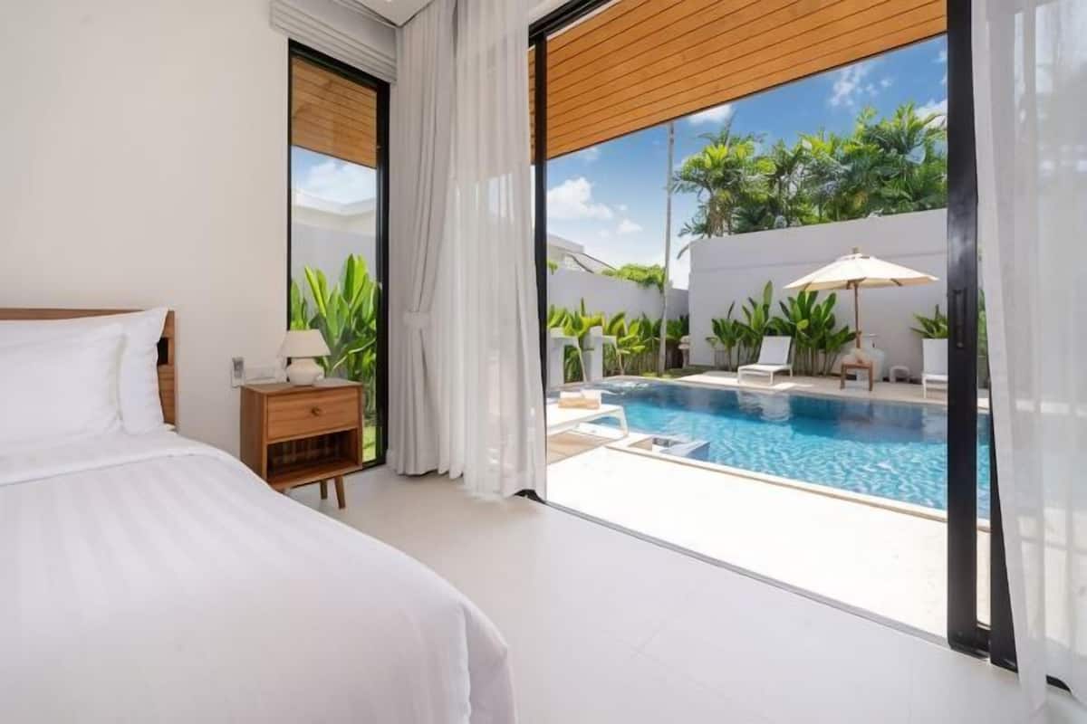 Una camera da letto con un letto grande, un comodino e vista su una piscina e un’area salotto all’aperto.