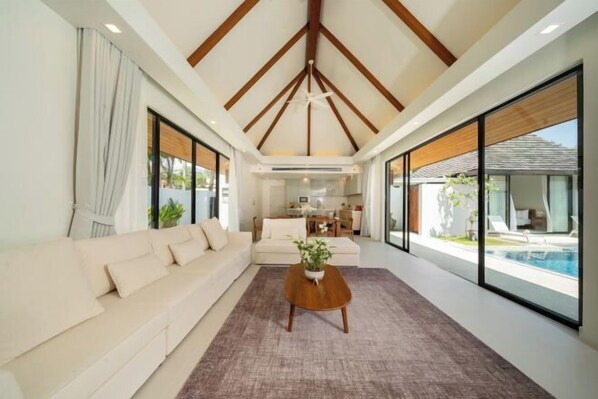 A modern living room with a sofa, a coffee table, and large windows. - Anchan Villas Phuket - Private 4 BR Signature Pool Villa by Escape Villas (Phuket)