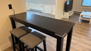 Una cocina moderna con encimera oscura, dos taburetes de bar, horno empotrado y televisor sobre un mueble.