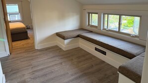 Una habitación con un banco empotrado junto a una ventana, una puerta que da a otra estancia y un cartel que señala un rincón de lectura.