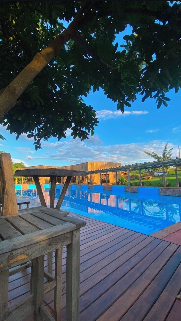 A wooden deck with a pool, a wooden pergola, and a view of a building in the background. - FAZENDA BROTAS (Brotas)