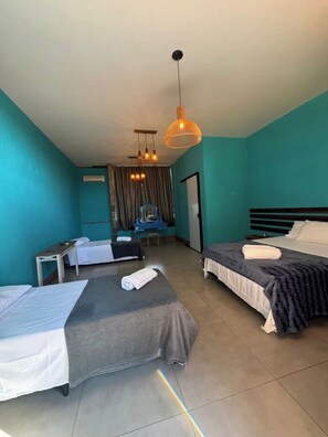 Une chambre d’hôtel avec deux lits, un bureau, une chaise, un luminaire suspendu et une fenêtre avec des rideaux.
