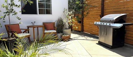 A patio with a grill, chairs, and potted plants.