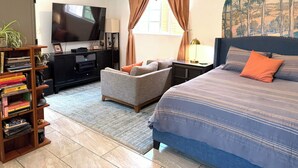 Quarto com uma cama, televisão, estante de livros e janela com cortinas.