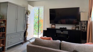 Sala de estar com um sofá cinza, televisão, armário e porta que dá para o exterior.
