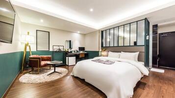 Habitación de hotel con una cama grande, un escritorio con computadora, una silla, una lámpara y un espejo.