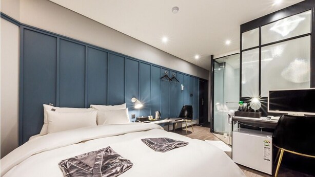 A modern hotel room with a large bed, a desk with a computer, a TV, and a wardrobe.
